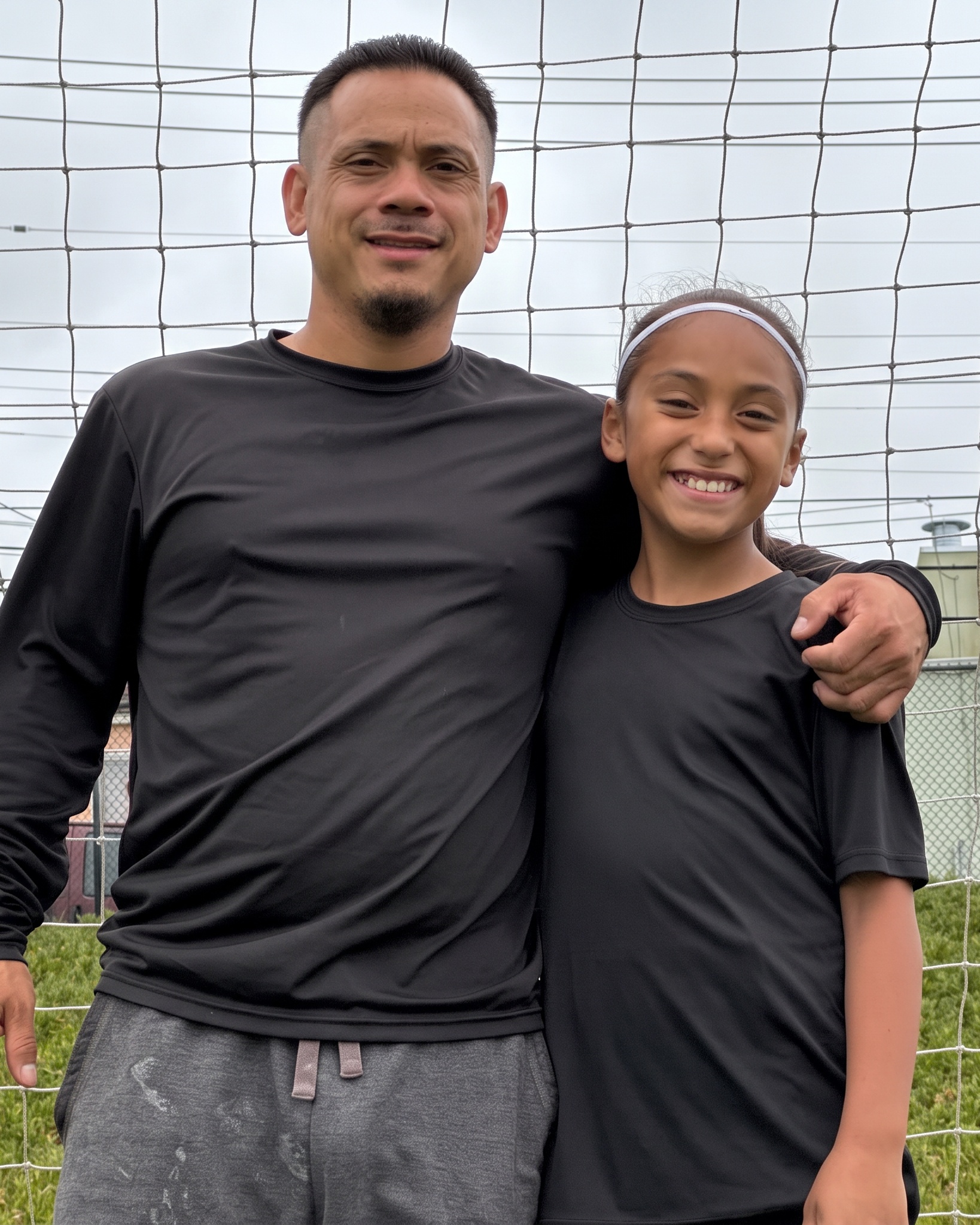 Dad and daughter smiling together in front of the soccer goal